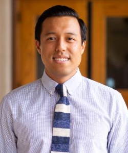 A photo of Dr. Leland Tabares. He is smiling at the camera, and wears a blue shirt and striped blue and white tie.