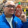 Photo of Dr. Martin Manalansan. He is wearing a blue jacket and is smiling while holding up a bottle of Sriracha Rooster Sauce.